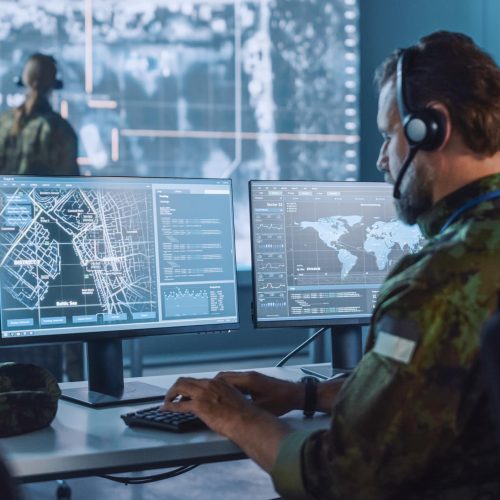 Military Surveillance Officer Working on a City Tracking Operation in a Central Office Hub for Cyber Control and Monitoring for Managing National Security, Technology and Army Communications.
